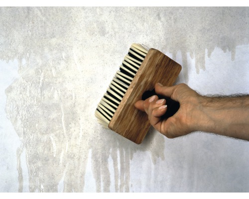 Main avec une brosse à tapisser sur du papier peint