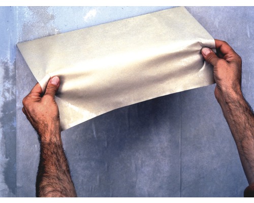 Une personne tient une feuille de papier contre un mur.