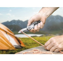 Une personne coupe une corde avec un couteau de poche dans la nature.