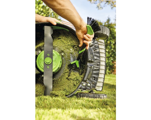Eine Person reinigt mit einer Bürste einen Rasenmäher von Grasresten.