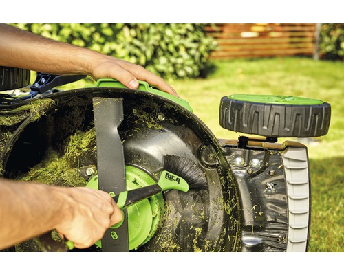 Eine Person reinigt mit einer Bürste einen Rasenmäher.