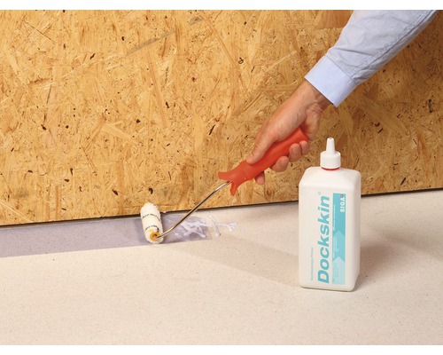 Une main applique de la colle avec un rouleau sur une structure en bois, avec un flacon de colle Siga Dockskin