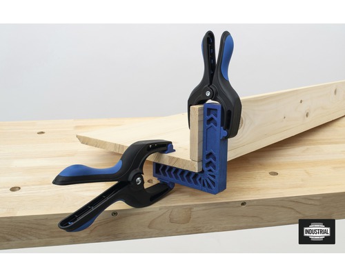 Deux serre-joints à ressort fixent des pièces de bois sur un établi.