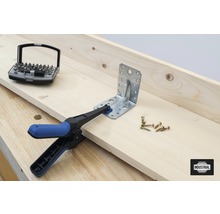 Winkelverbinder wird mit Schraubzwinge auf Holzstück fixiert, Schrauben und Bit-Set liegen bereit.