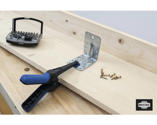 Winkelverbinder wird mit Schraubzwinge auf Holzstück fixiert, Schrauben und Bit-Set liegen bereit.