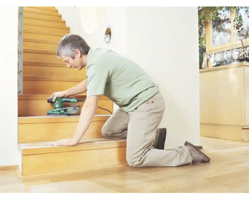 Un homme ponce un escalier en bois avec une ponceuse.
