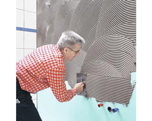 Un homme applique de la colle à carrelage sur un mur à l''aide d''une truelle.