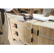 Handwerker arbeitet mit einer Lamellofräse an einem Holzmöbelstück, das mit Schraubzwingen fixiert ist.