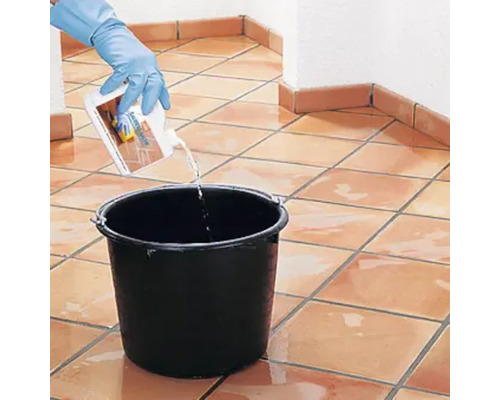 Eine Person mit Handschuhen giesst Reiniger in einen Eimer auf einem gefliesten Boden.