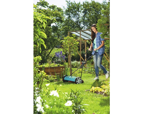 Une femme utilise une tondeuse à gazon manuelle dans le jardin