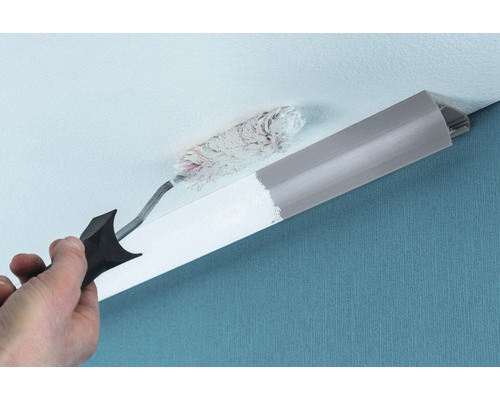 Eine Person streicht eine Zierleiste mit einem Farbroller an einer Zimmerdecke.