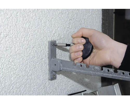 Eine Person befestigt mit einem Schraubendreher einen Metall-Wäscheständer an einer Wand.