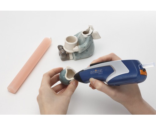 Une personne répare une figurine en céramique avec un pistolet à colle chaude Steinel.