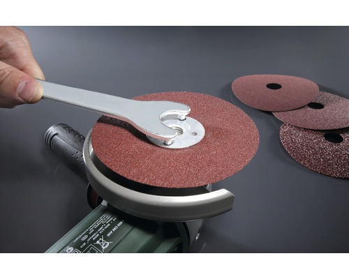 Une meuleuse d''angle avec du papier abrasif monté et une clé pour remplacer le papier abrasif.
