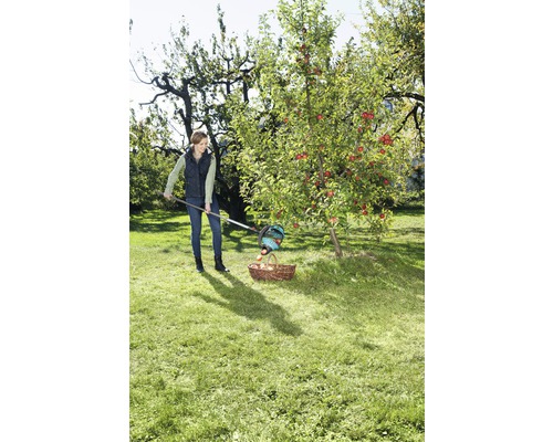 Frau erntet Äpfel mit einem Obstpflücker und einem Korb im Garten.