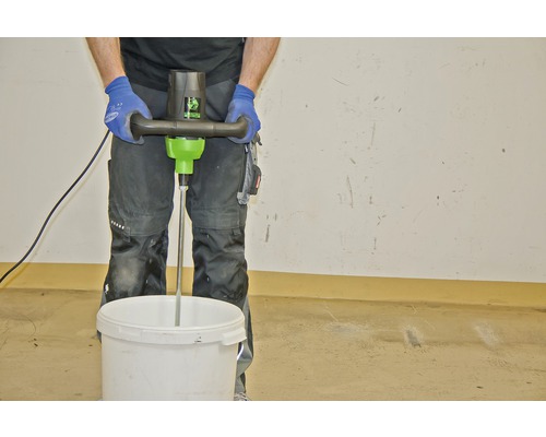 Un artisan mélange des matériaux avec un mélangeur électrique dans un seau.