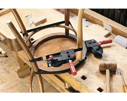 Une chaise en bois est réparée avec un tendeur à sangle sur un établi