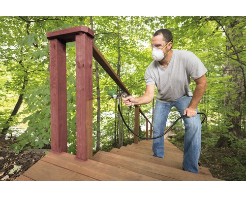 Un homme peint un escalier extérieur en bois avec un pulvérisateur de peinture