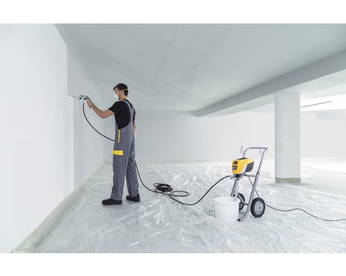 Un homme peint un mur avec un pulvérisateur de peinture dans un intérieur