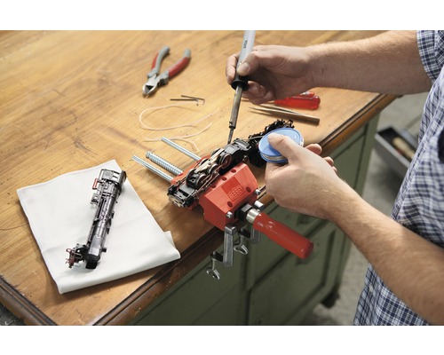 Une personne répare un train miniature avec un fer à souder et un serre-joint