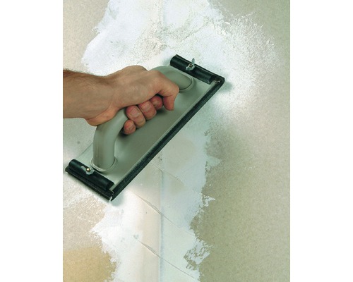 Main avec une taloche appliquant du plâtre sur un mur