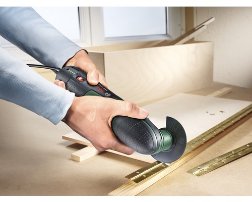 Un homme travaille sur une pièce de bois avec un outil multifonctionnel, des charnières étant placées à l''arrière-plan.