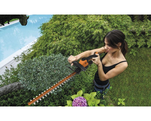 Une femme taille une haie avec un taille-haie dans le jardin