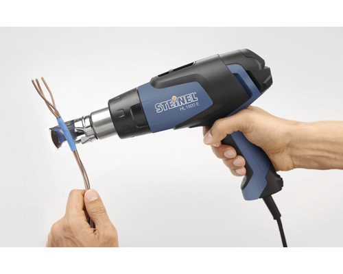 Une main tient un pistolet thermique et chauffe un câble.