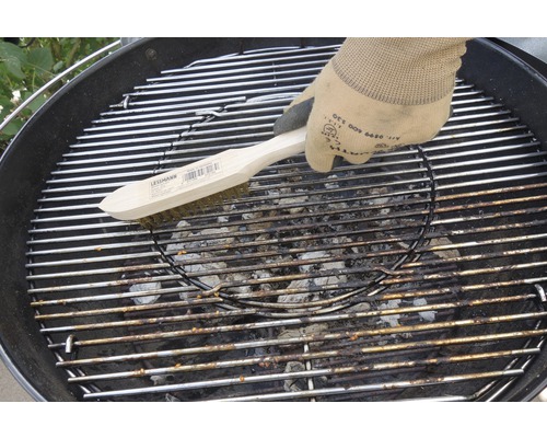 Eine Person reinigt einen Grillrost mit einer Drahtbürste.