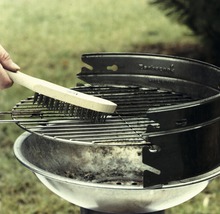 Eine Person reinigt einen Grillrost mit einer Grillbürste mit Holzgriff.