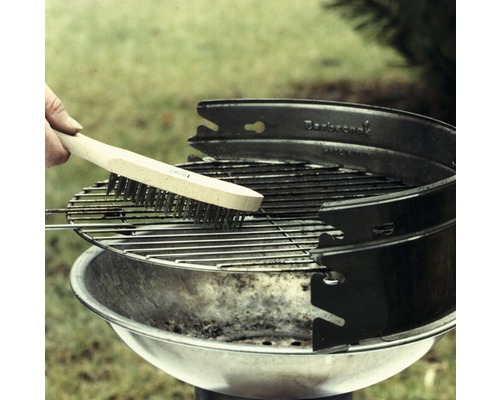 Eine Person reinigt einen Grillrost mit einer Grillbürste mit Holzgriff.