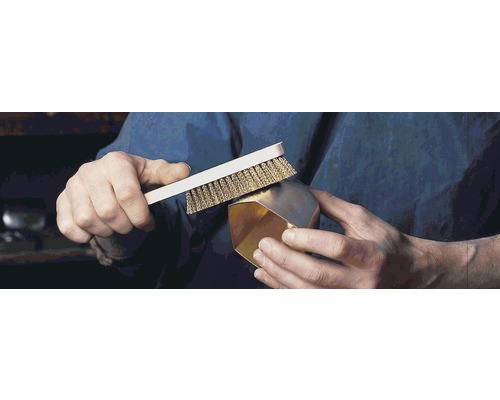 Une personne nettoie un objet doré avec une brosse métallique.