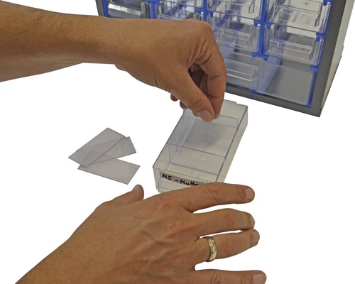 Eine Person befüllt eine Schublade eines Sortimentskasten mit Etiketten.