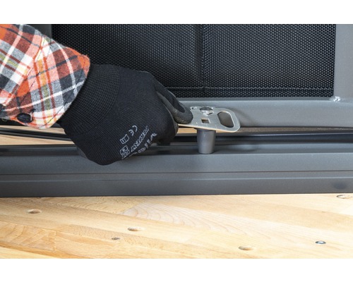 Eine Person befestigt eine silberfarbene Metallhalterung an einem Fenstergitter.