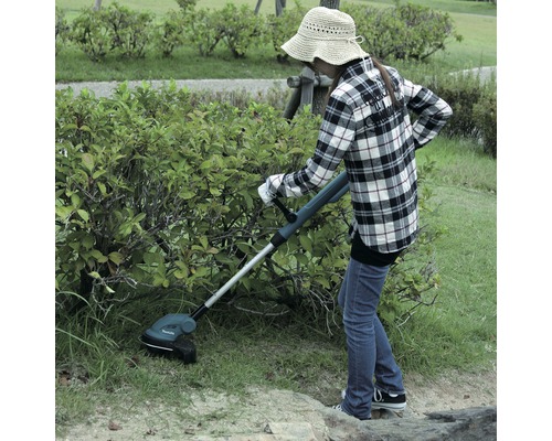 Une femme coupe l''herbe dans le jardin avec un coupe-bordures sans fil.