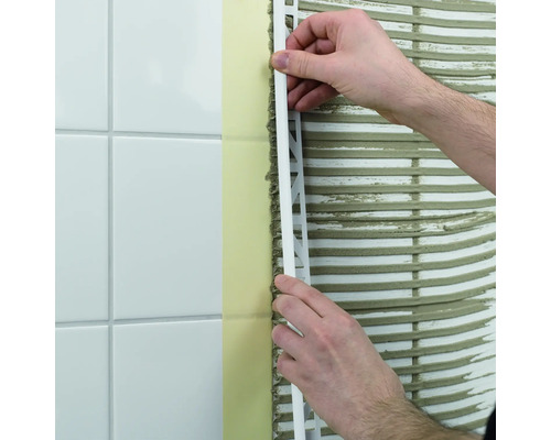 Un homme fixe un profilé de carrelage sur un mur carrelé.