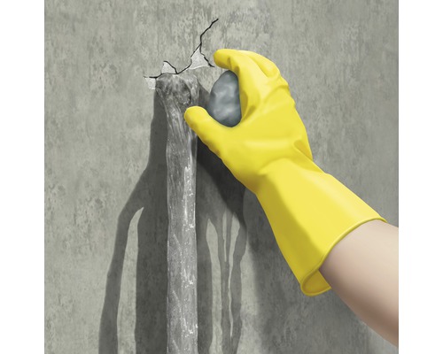 Hand mit Handschuh dichtet Riss in einer Wand ab, aus dem Wasser austritt