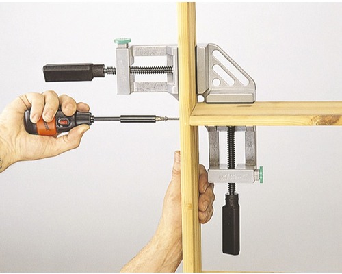 Zwei Eckspannzwingen fixieren Holz während des Verschraubens mit einem Schraubendreher.