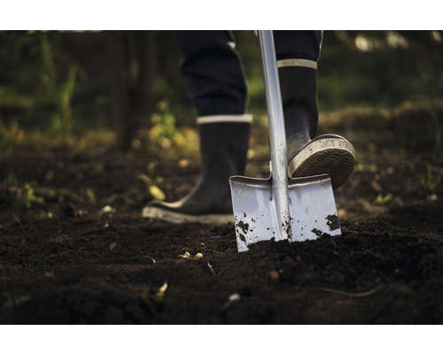 Une personne en bottes en caoutchouc utilise une bêche dans le jardin.