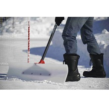 Person schiebt Schnee mit einem Schneeschieber auf einer Eisfläche.