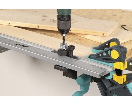 Une perceuse avec un gabarit de perçage de goujons perçant une planche de bois avec des serre-joints à goujons Wolfcraft.