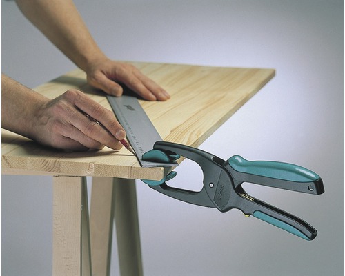 Un homme marque une planche de bois avec un crayon et une équerre de butée, fixée avec une serre-joint à une main sur une table