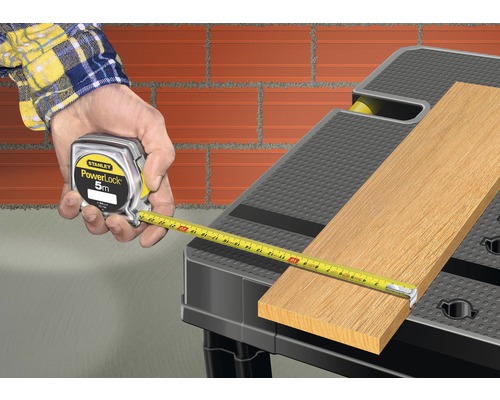 Un artisan mesure du bois avec un mètre Stanley PowerLock sur un établi.