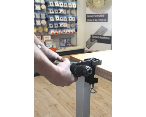 Ein Mann befestigt eine Bohrmaschine mit einer Tischhalterung an einer Tischplatte.