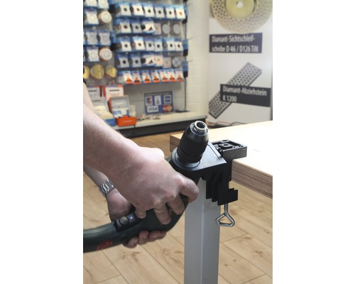 Eine Bohrmaschine mit Bohrständer ist an einer Tischplatte befestigt.