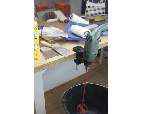 Ein grüner Bohrmaschinenmischer mit rotem Rührwerk in einem schwarzen Eimer auf einem Tisch mit Werkzeugen.