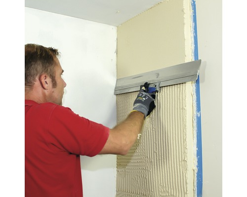 Un homme lisse du plâtre avec une spatule sur un mur. L''image montre l''application d''enduit à l''intérieur.