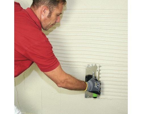 Un homme applique du plâtre sur un mur avec une taloche