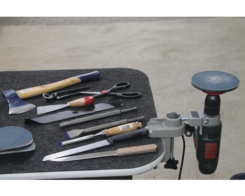 Verschiedene Werkzeuge, darunter eine Axt, Meißel und eine Bohrmaschine mit Schleifscheibe, liegen auf einem Tisch.