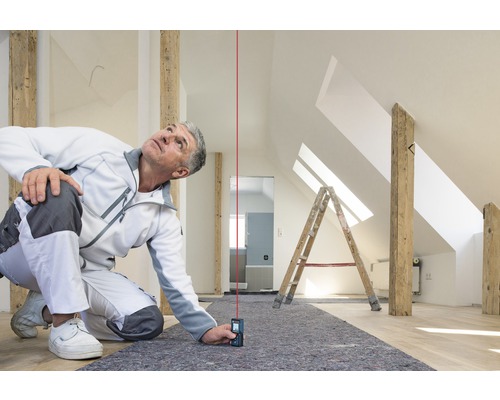 Un artisan utilise un télémètre laser dans un grenier pour effectuer des mesures précises.